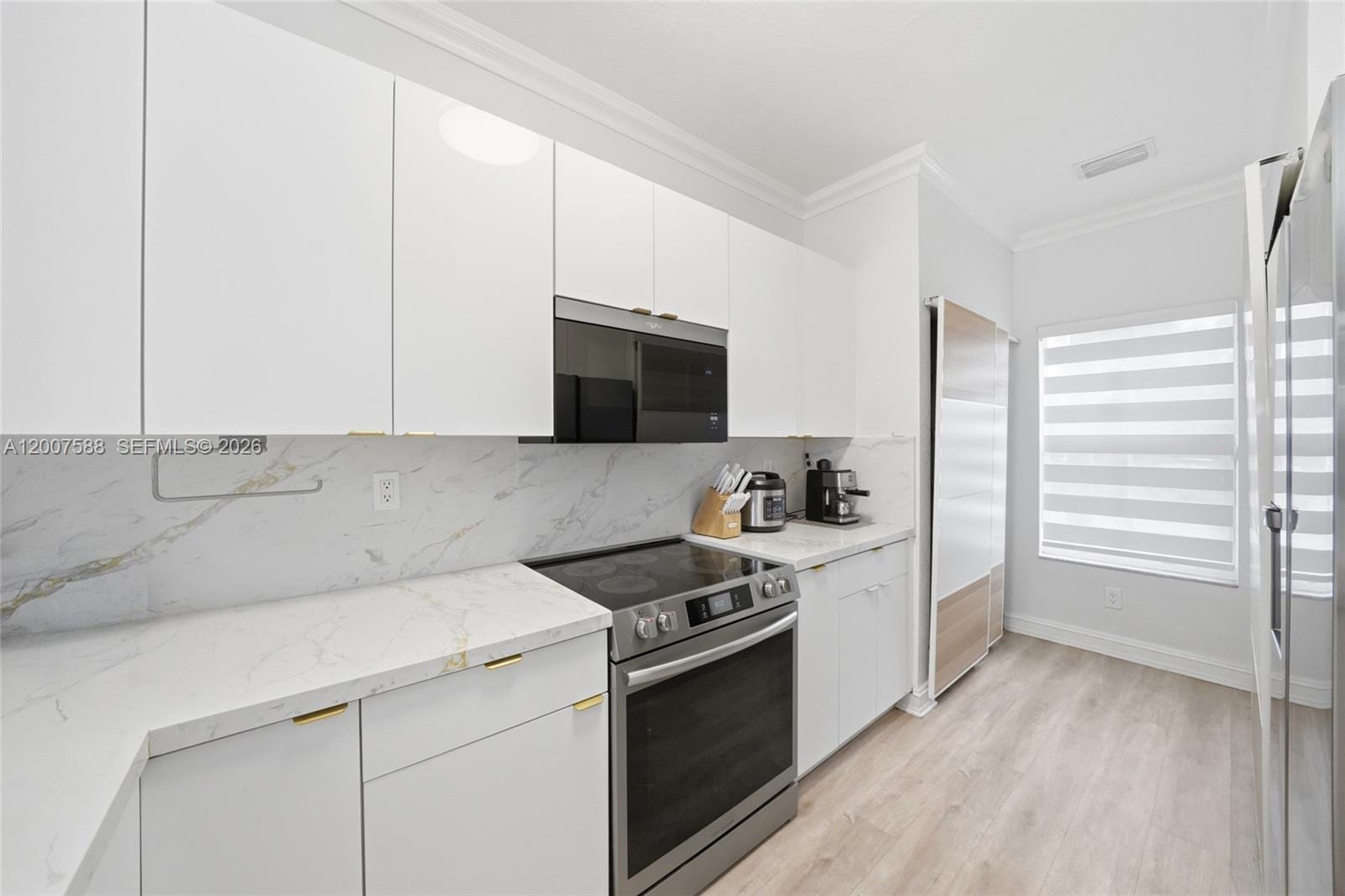 A modern kitchen features white cabinets, marble-style countertops, stainless steel appliances, and light wood flooring — MIRAMAR, FL
