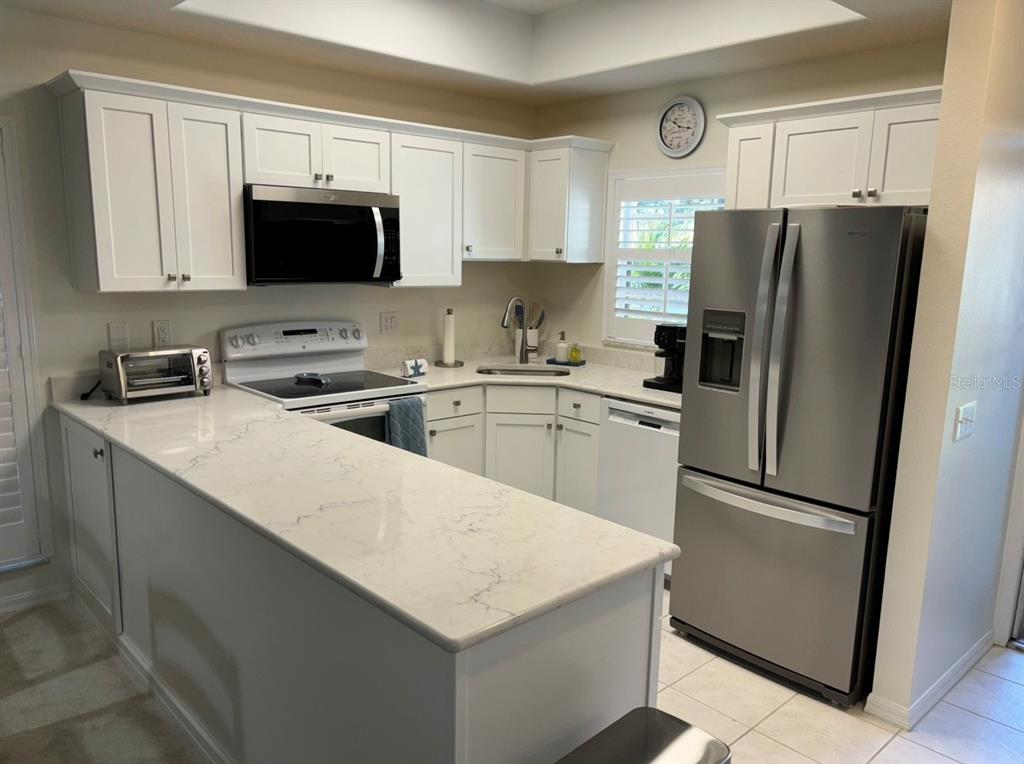 A kitchen features white cabinets, stainless steel appliances, and a white quartz countertop peninsula — 8369 WINGATE DRIVE UNIT 2114, SARASOTA, FL