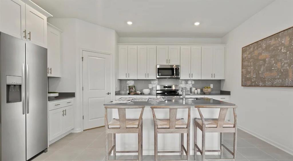 A modern kitchen features white cabinetry, stainless steel appliances, a center island, and bar stools — 4246 ST THOMAS WAY, KISSIMMEE, FL