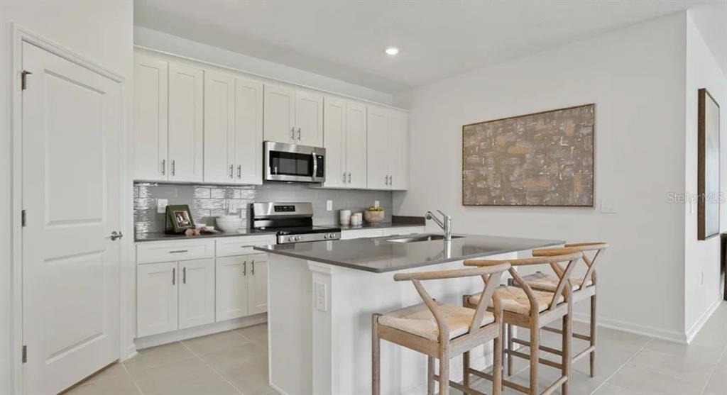 A modern kitchen features white cabinets, a gray island with bar stools, and stainless appliances — 4246 ST THOMAS WAY, KISSIMMEE, FL