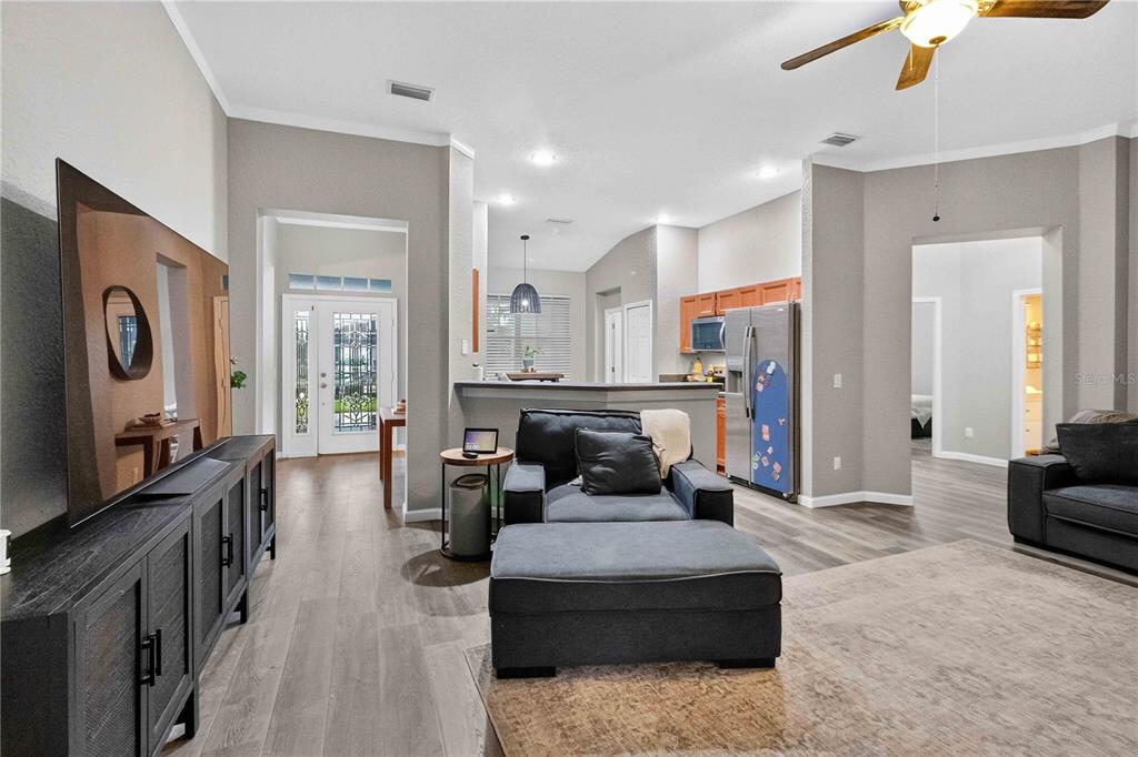 A living room with gray flooring, a large television, and an open kitchen in the background — 11326 LAUREL BROOK COURT, RIVERVIEW, FL