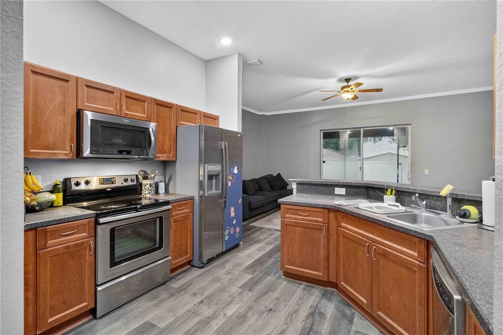 A kitchen with wood cabinets, stainless steel appliances, and gray countertops opens to a living area — 11326 LAUREL BROOK COURT, RIVERVIEW, FL