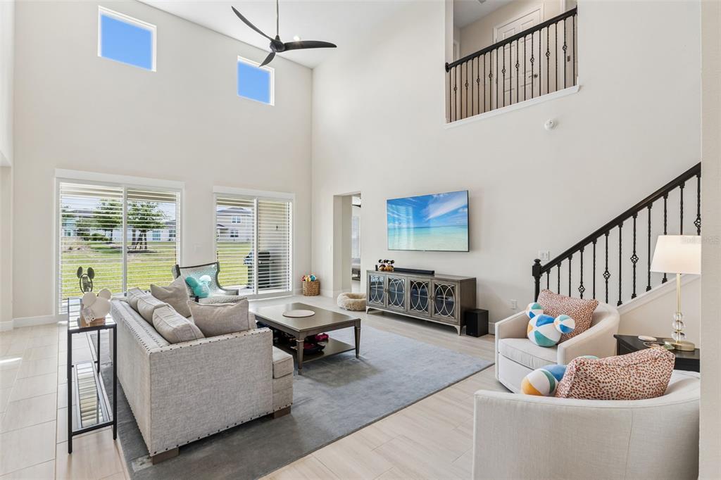 A living room features high ceilings, a staircase, large windows, and neutral furniture — 14321 CRESTAVISTA AVENUE, CLERMONT, FL