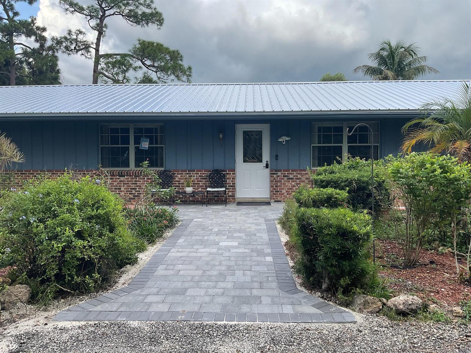 A blue house with a metal roof, brick base, and a gray paver walkway — 3208 A Road, FL 33470, FL