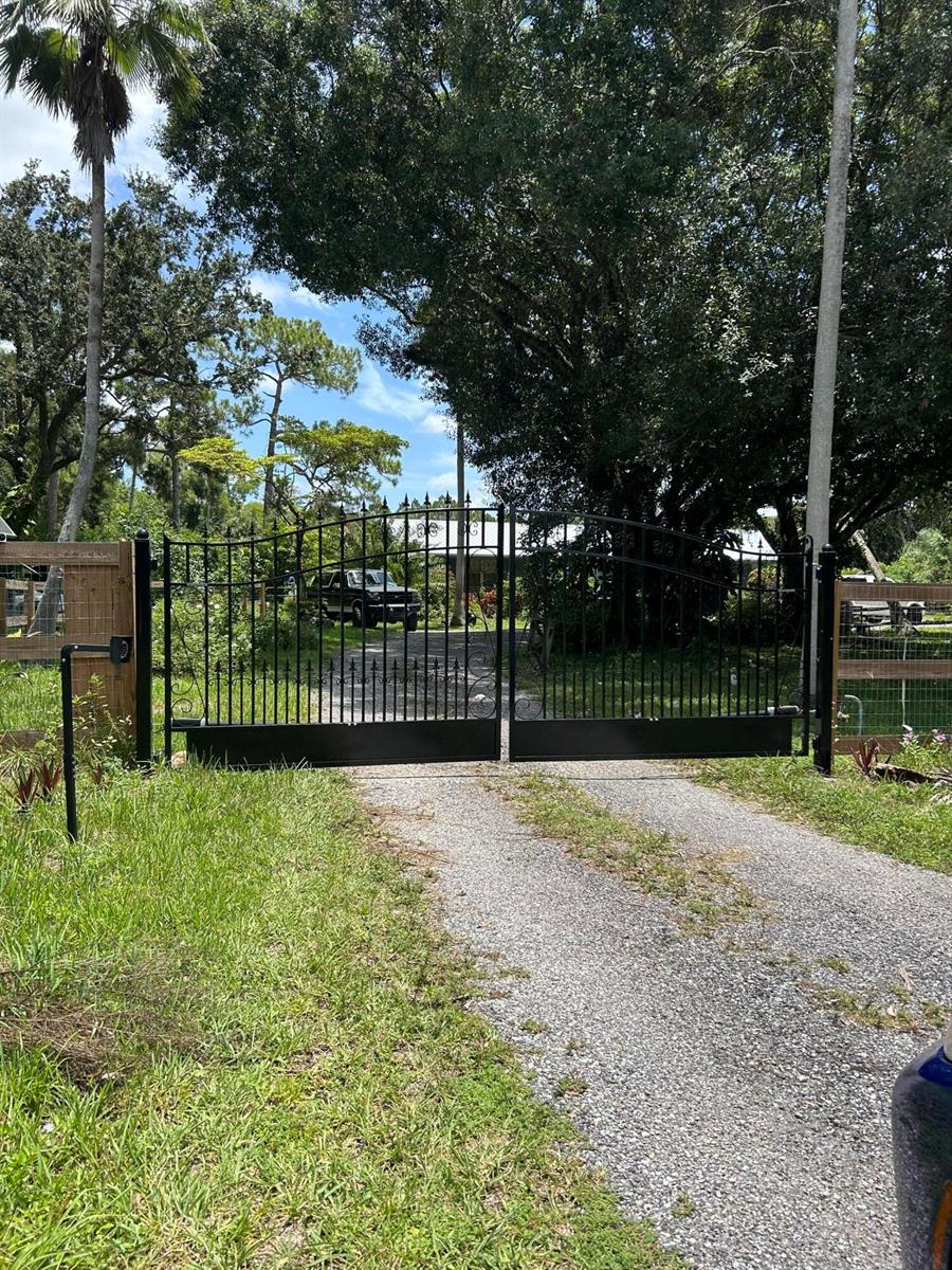 A black metal driveway gate stands at the entrance of a gravel path — 3208 A Road, FL 33470, FL