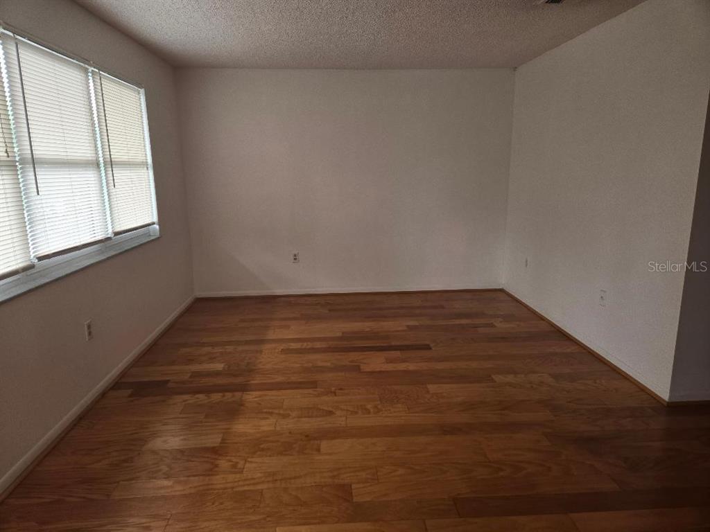 An empty room features light-colored walls, a window with blinds, and hardwood flooring — 3128 59TH STREET S UNIT 205, GULFPORT, FL