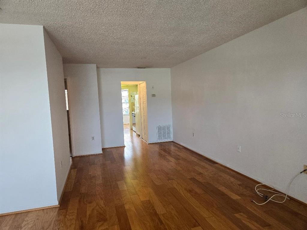 An empty room with wood-look flooring and a doorway leading to a kitchen area — 3128 59TH STREET S UNIT 205, GULFPORT, FL