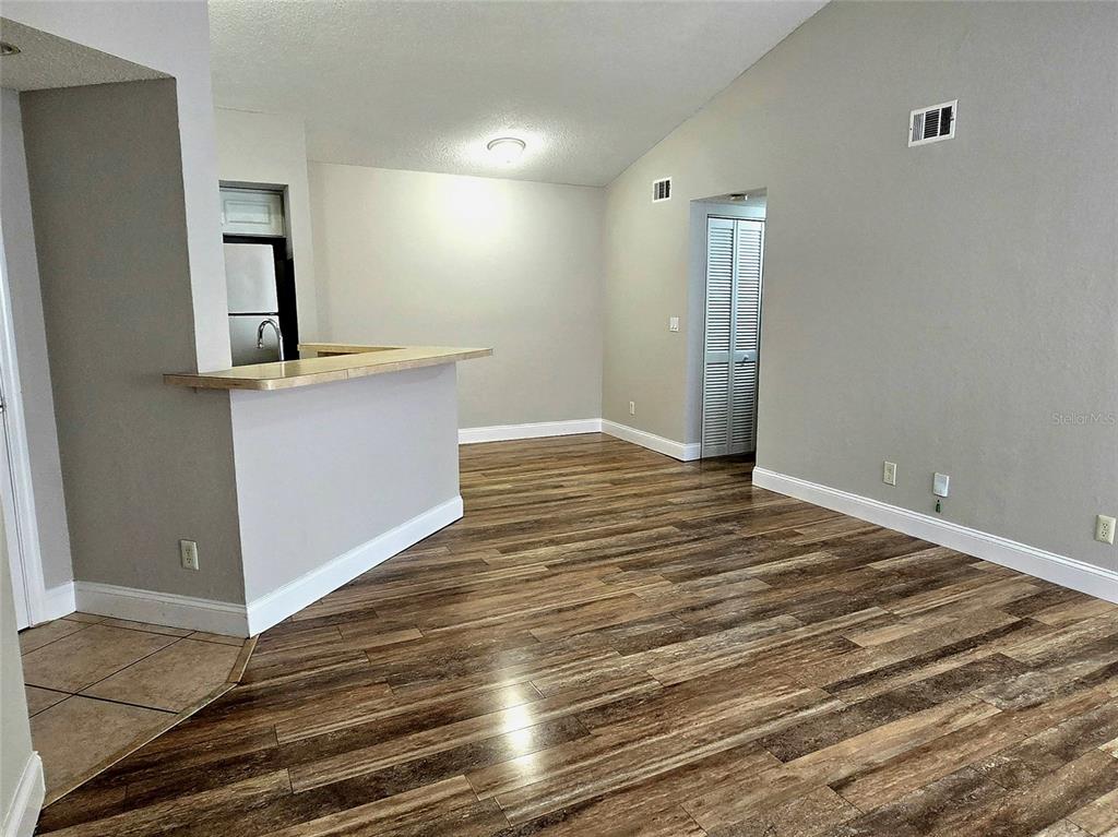 An open-concept living area features wood-look flooring, a breakfast bar, and a vaulted ceiling — 4630 COMMANDER DRIVE UNIT 1038, ORLANDO, FL