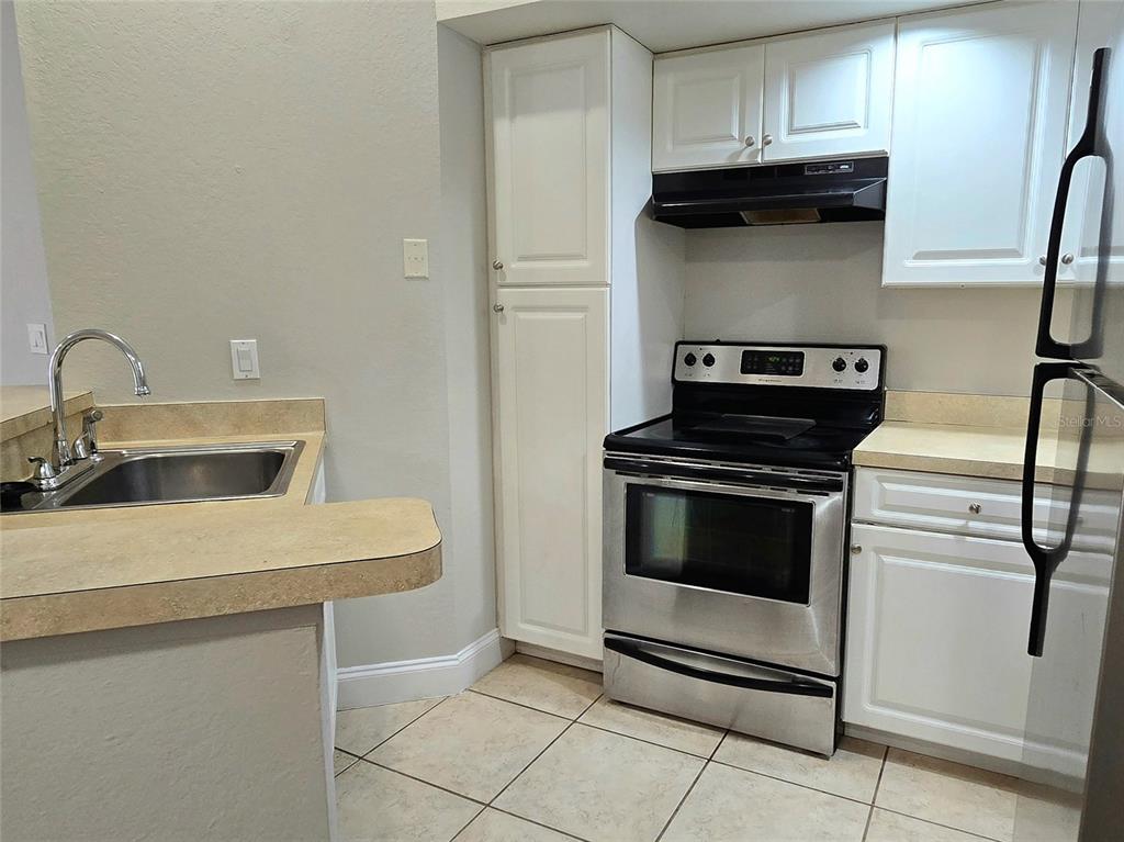 A kitchen features white cabinets, a stainless steel stove, and tan laminate countertops — 4630 COMMANDER DRIVE UNIT 1038, ORLANDO, FL