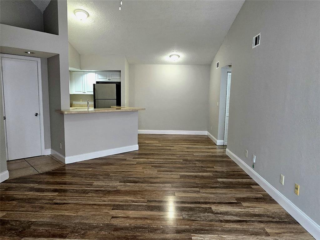 An open-concept living area features wood-look flooring, a kitchen breakfast bar, and vaulted ceilings — 4630 COMMANDER DRIVE UNIT 1038, ORLANDO, FL