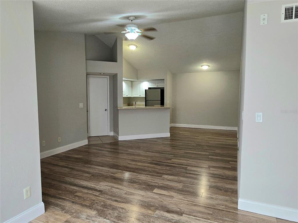 An open-concept living area features wood-look flooring, a vaulted ceiling, and a kitchen with white cabinets — 4630 COMMANDER DRIVE UNIT 1038, ORLANDO, FL