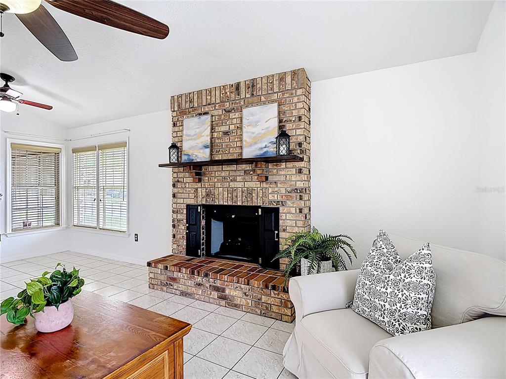 A living room features a brick fireplace, a wooden mantel, tiled floors, and a sofa — 1144 MONROE AVENUE, ST CLOUD, FL