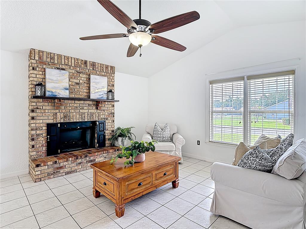 A living room features a brick fireplace, tile flooring, a ceiling fan, and white furniture — 1144 MONROE AVENUE, ST CLOUD, FL
