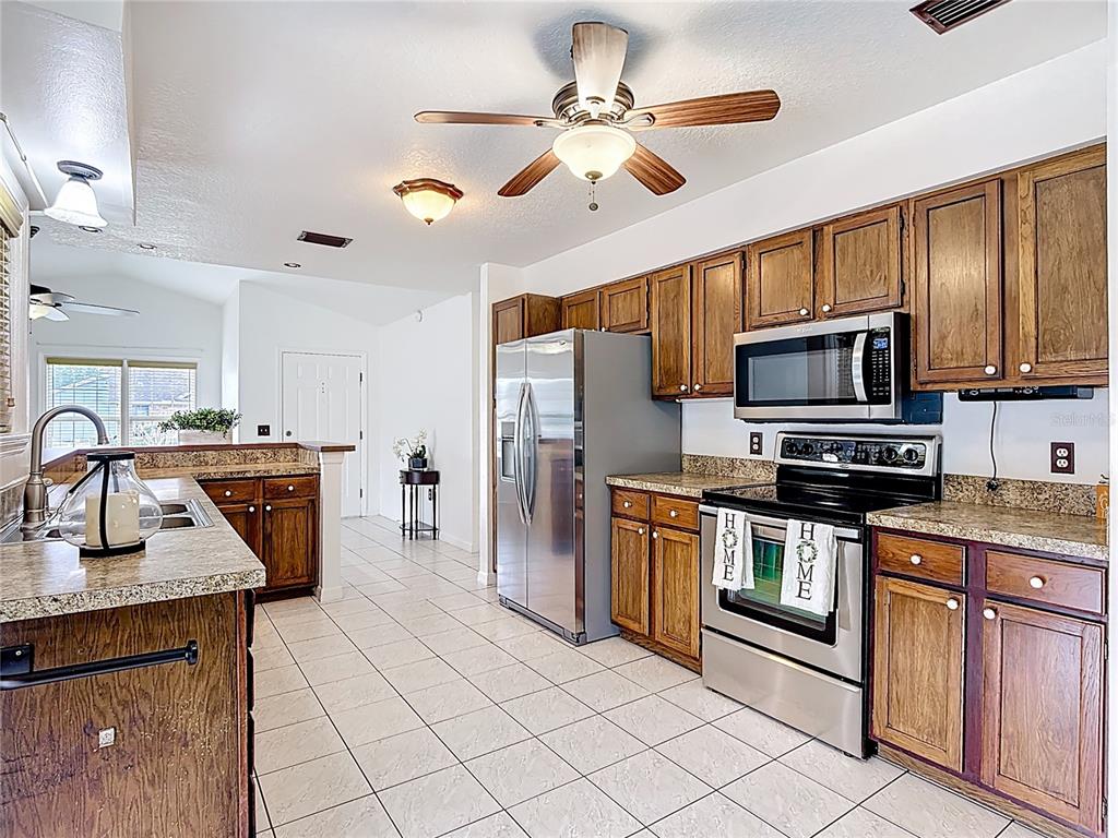A kitchen features wood cabinets, granite countertops, stainless steel appliances, and light-colored tile flooring — 1144 MONROE AVENUE, ST CLOUD, FL