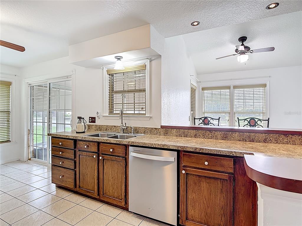 A kitchen features wood cabinets, granite countertops, a stainless steel dishwasher, and tile flooring — 1144 MONROE AVENUE, ST CLOUD, FL