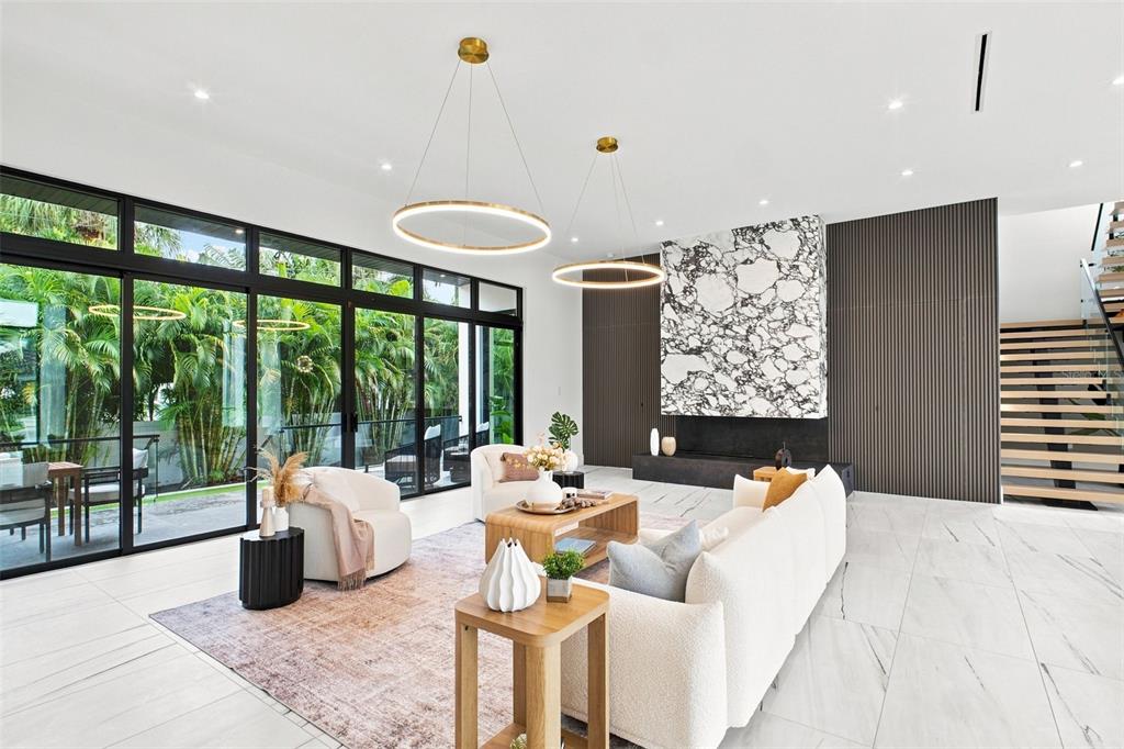 A modern living room features a marble fireplace, large glass doors, and a floating staircase — 1076 SNELL ISLE BOULEVARD NE, ST PETERSBURG, FL