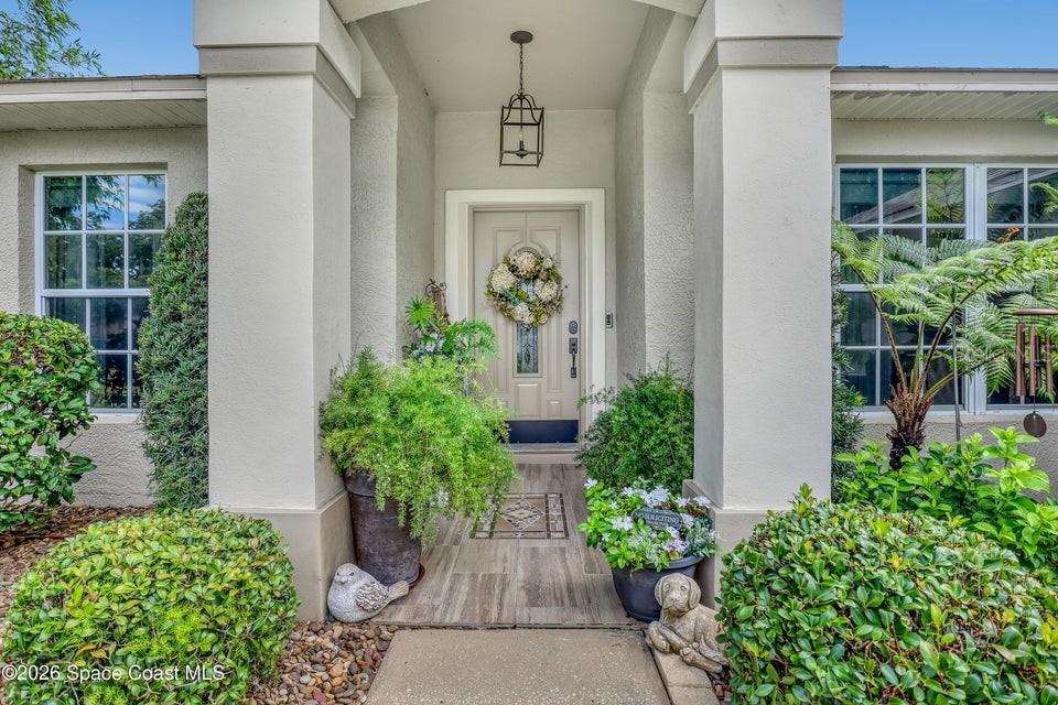 A covered front entryway features a light-colored door with a wreath and potted plants — 5515 OAK HOLLOW DRIVE, TITUSVILLE, FL
