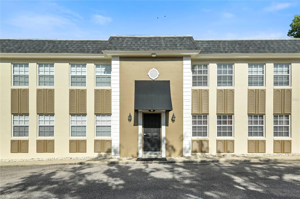 A two-story apartment building exterior features tan walls, brown shutters, and a central black awning — 317 E AMELIA STREET UNIT 7, ORLANDO, FL