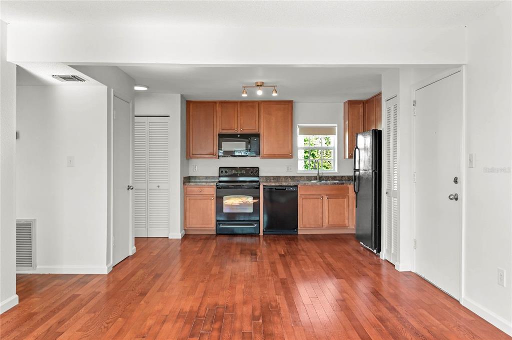 A kitchen with wood cabinets, black appliances, and hardwood floors opens to a living area — 317 E AMELIA STREET UNIT 7, ORLANDO, FL