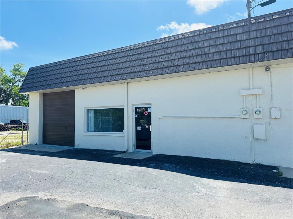 A single-story commercial building with a dark brown roof, a garage door, and an entrance — 7904 US HIGHWAY 19, PORT RICHEY, FL