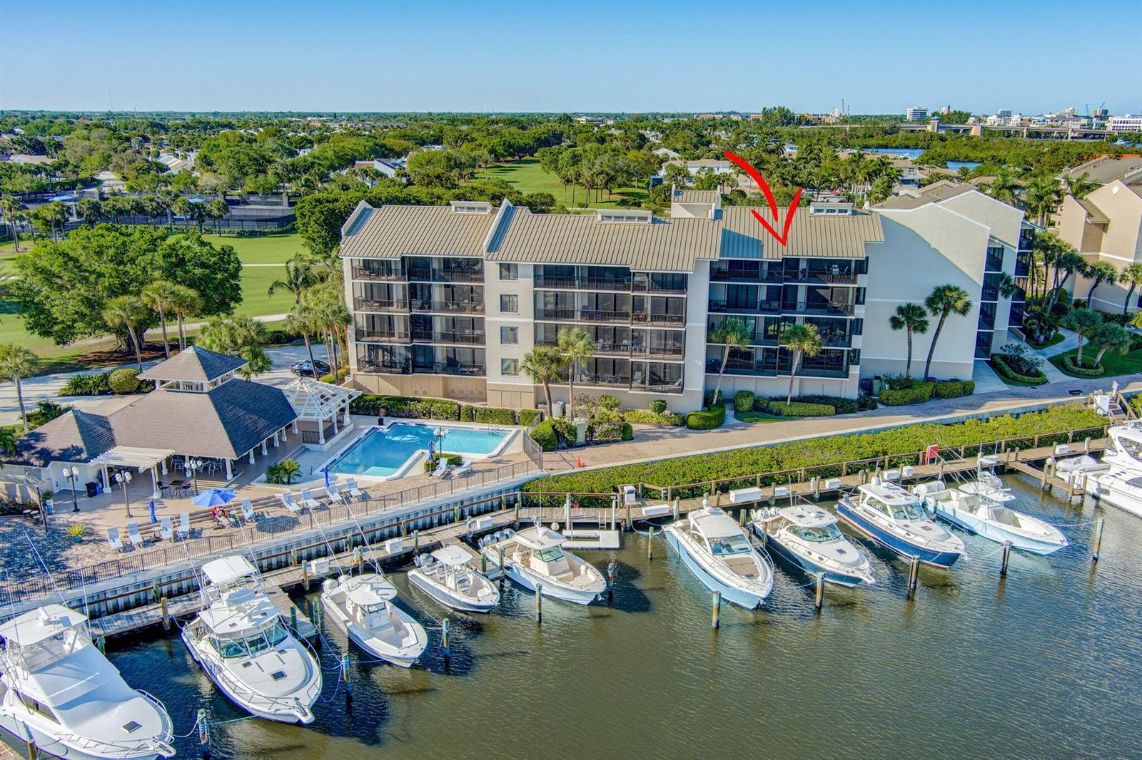 An aerial view shows a multi-story waterfront condominium building with a pool and boat slips — 16910 Bay Street E # E503, Jupiter FL 33477, JUPITER, FL
