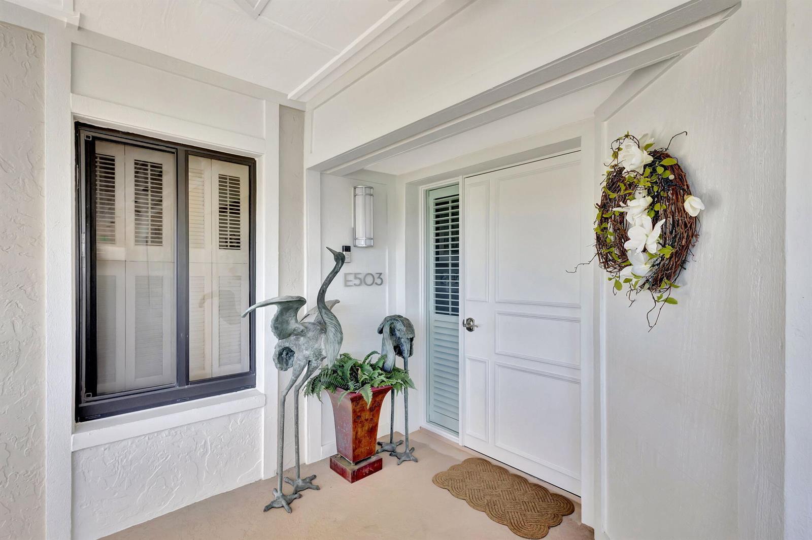 A white front door with a side window and two bird statues on a porch — 16910 Bay Street E # E503, Jupiter FL 33477, JUPITER, FL