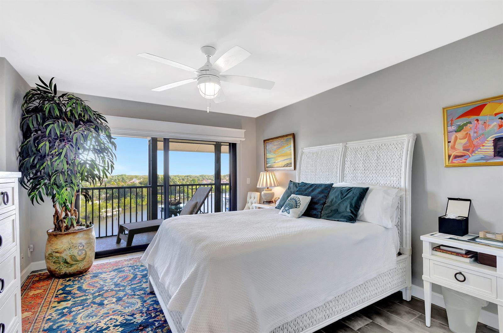 A bedroom features a white wicker bed, a large potted plant, and a balcony view — 16910 Bay Street E # E503, Jupiter FL 33477, JUPITER, FL