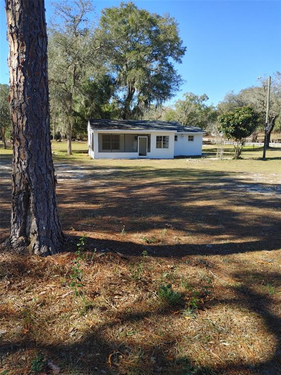 A white single-story house with a screened-in porch sits on a large, grassy lot — 1838 NE 145TH AVENUE ROAD, SILVER SPRINGS, FL
