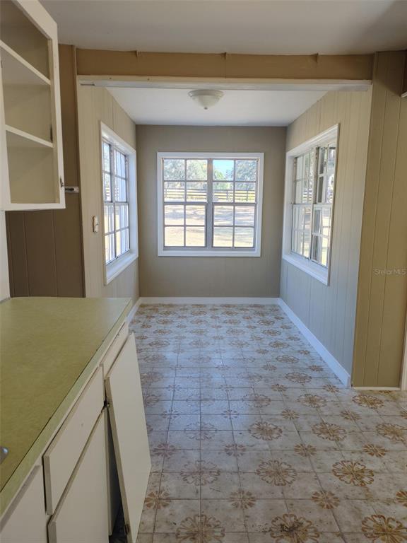A kitchen nook features patterned tile flooring, wood-paneled walls, and three windows overlooking a yard — 1838 NE 145TH AVENUE ROAD, SILVER SPRINGS, FL
