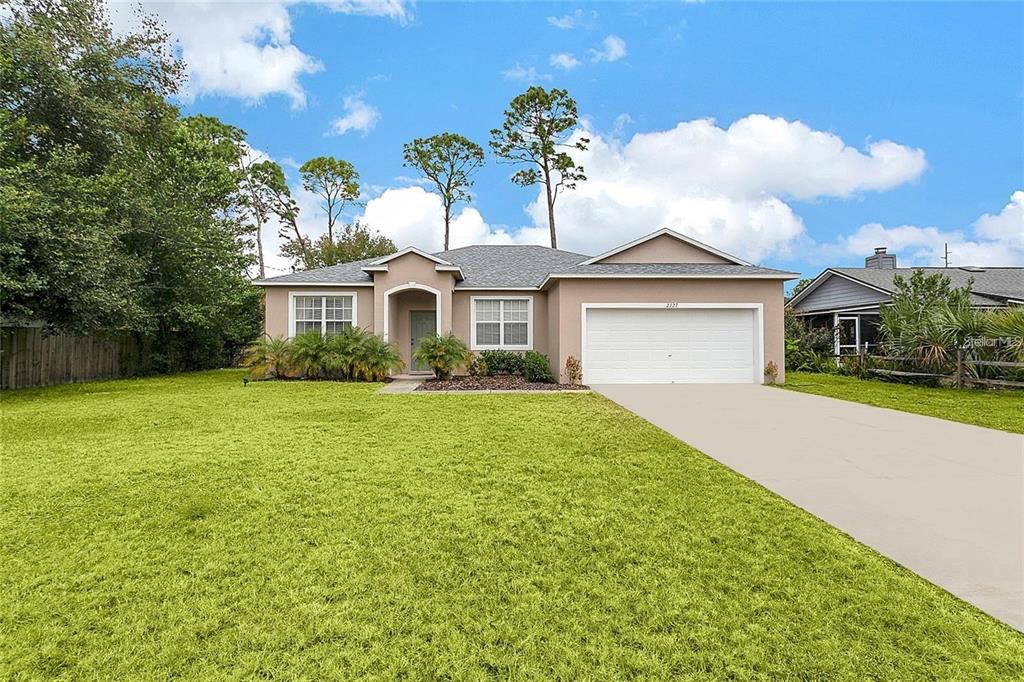 A single-story house with a beige stucco exterior, a two-car garage, and a large lawn — 2727 RAMSEY DRIVE, APOPKA, FL