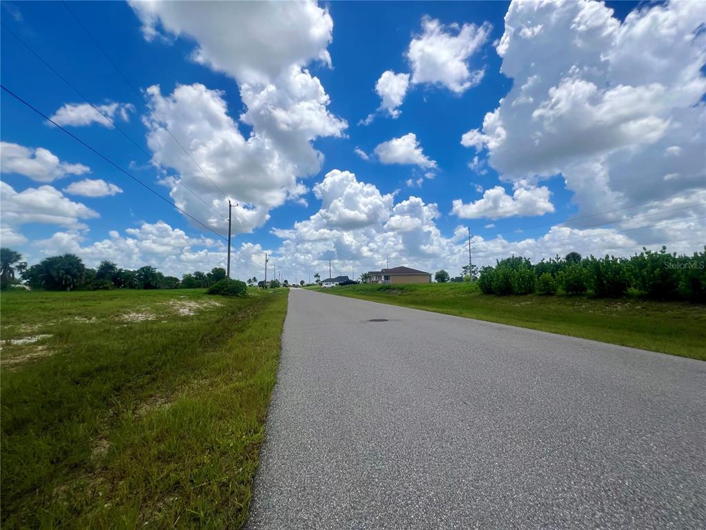 A paved road stretches into the distance between grassy lots under a bright, cloudy sky — 1423 NW 8TH TERRACE, CAPE CORAL, FL