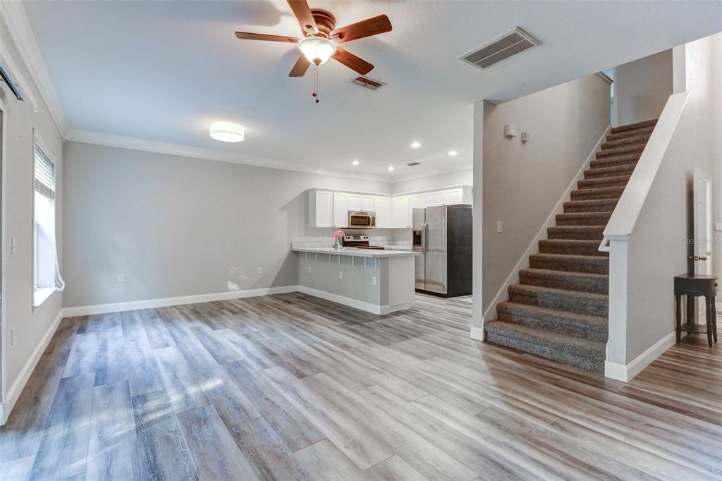 An open-concept living area features wood-look flooring, a kitchen with white cabinets, and carpeted stairs — 16305 FAIRFORD PALMS COURT, TAMPA, FL