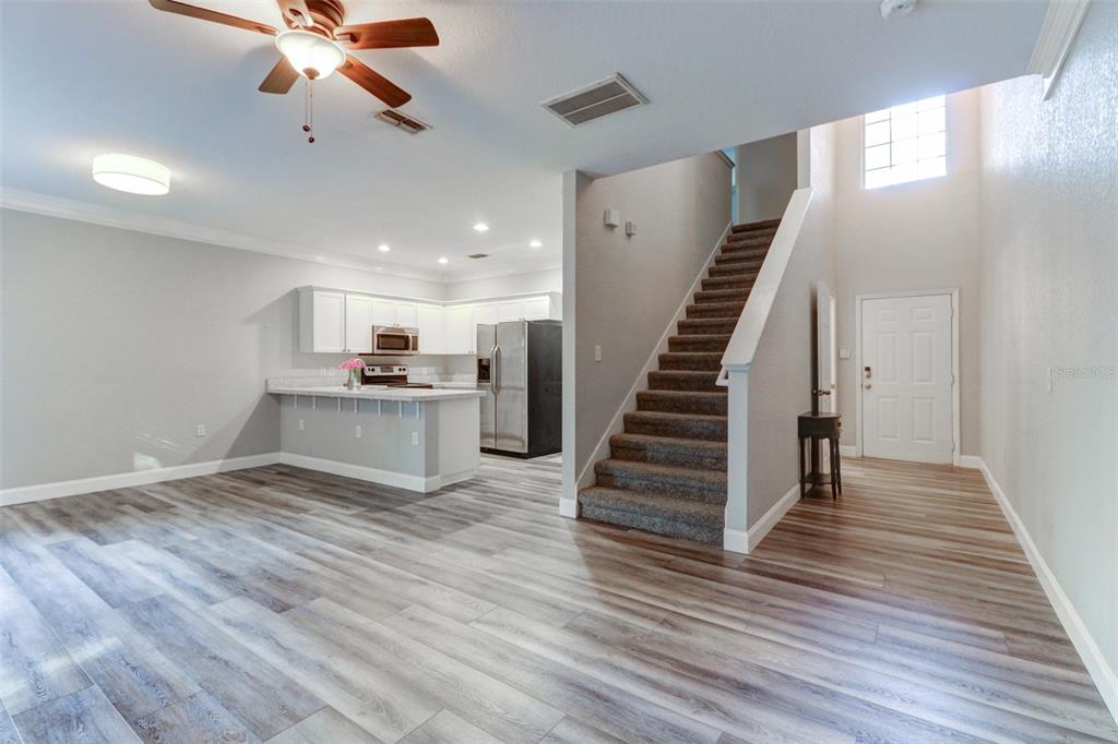 An open-concept living area features wood-look flooring, a kitchen with white cabinets, and carpeted stairs — 16305 FAIRFORD PALMS COURT, TAMPA, FL