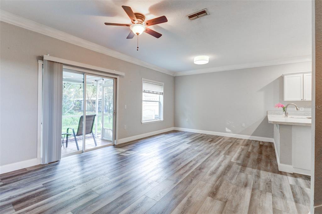 An open-concept living area features wood-look flooring, a ceiling fan, and sliding glass patio doors — 16305 FAIRFORD PALMS COURT, TAMPA, FL