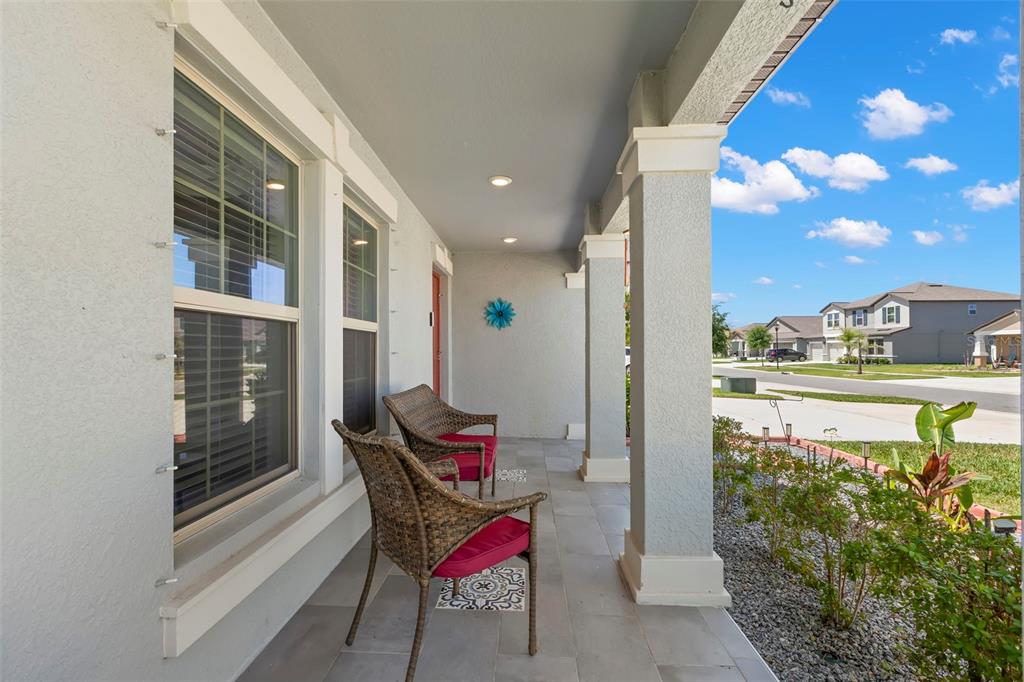 A covered front porch features tiled flooring, two wicker chairs, and square support columns — 13511 WILLOW BLUESTAR LOOP, RIVERVIEW, FL