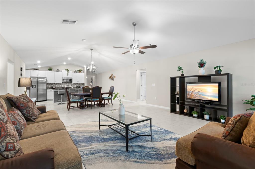 A living room with a glass coffee table, brown sofas, and an open-concept kitchen — 13511 WILLOW BLUESTAR LOOP, RIVERVIEW, FL