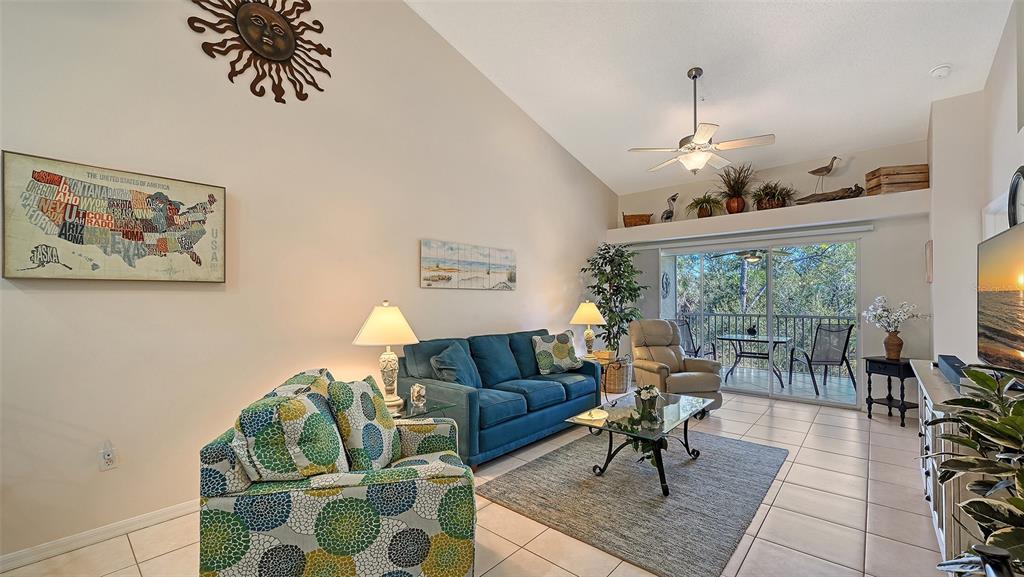 A living room features a blue sofa, patterned armchair, vaulted ceiling, and a sliding glass door — 4655 TOWER HILL LANE UNIT 2422, SARASOTA, FL