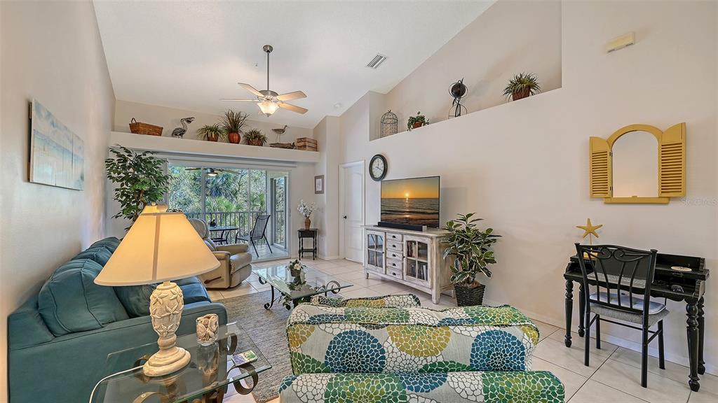 A living room features a blue sofa, patterned armchairs, a television, and a balcony view — 4655 TOWER HILL LANE UNIT 2422, SARASOTA, FL