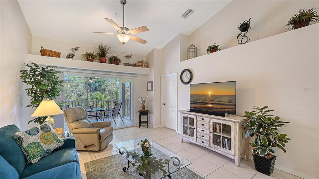 A living room features a vaulted ceiling, tile flooring, a television console, and a balcony — 4655 TOWER HILL LANE UNIT 2422, SARASOTA, FL