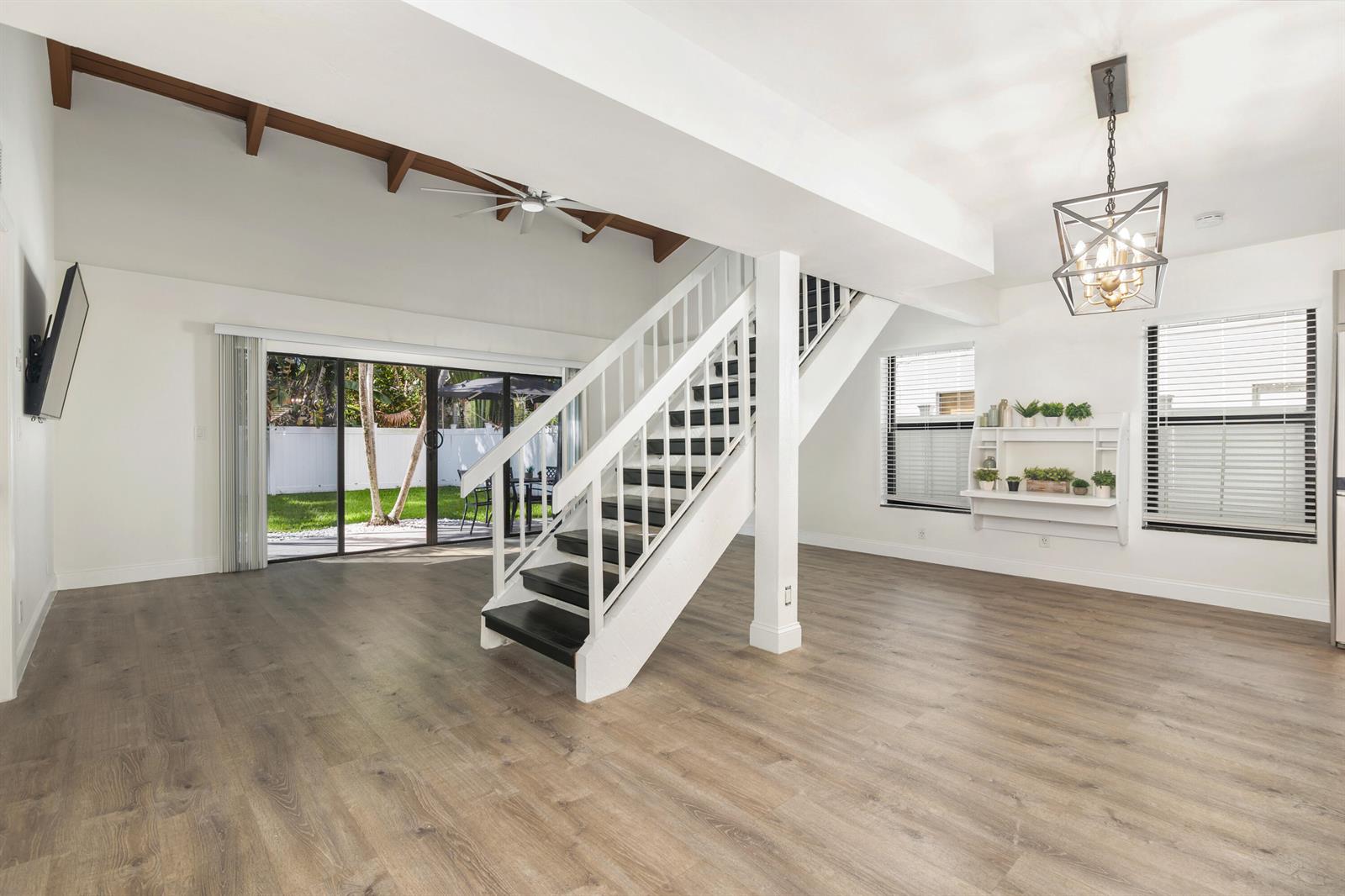 An open living area features wood-look flooring, a central staircase, and sliding glass doors to a yard — 2474 Douglas Avenue, Delray Beach FL 33444, DELRAY BEACH, FL