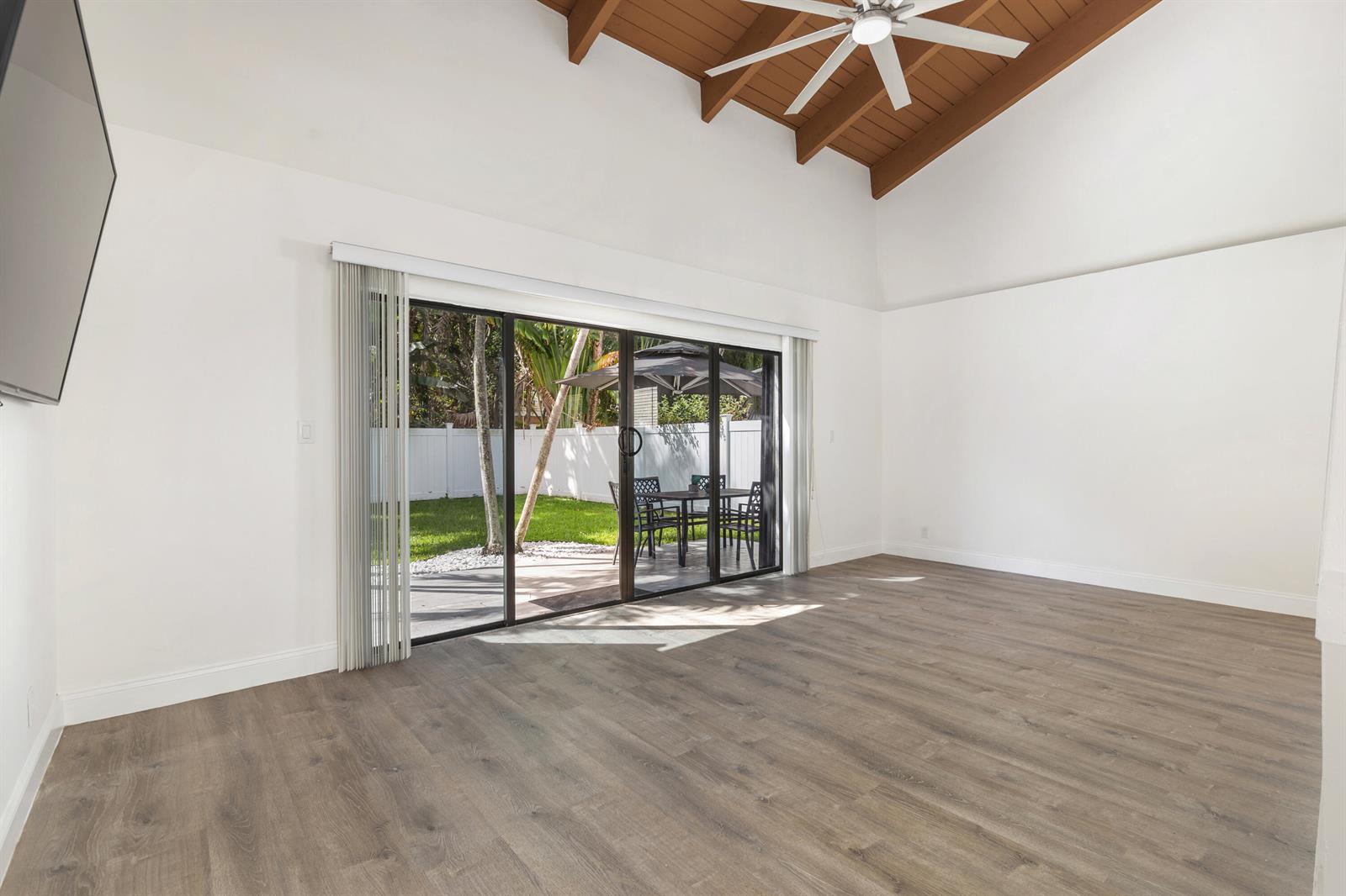 A living room features wood-look flooring, a vaulted ceiling with exposed beams, and sliding glass doors — 2474 Douglas Avenue, Delray Beach FL 33444, DELRAY BEACH, FL