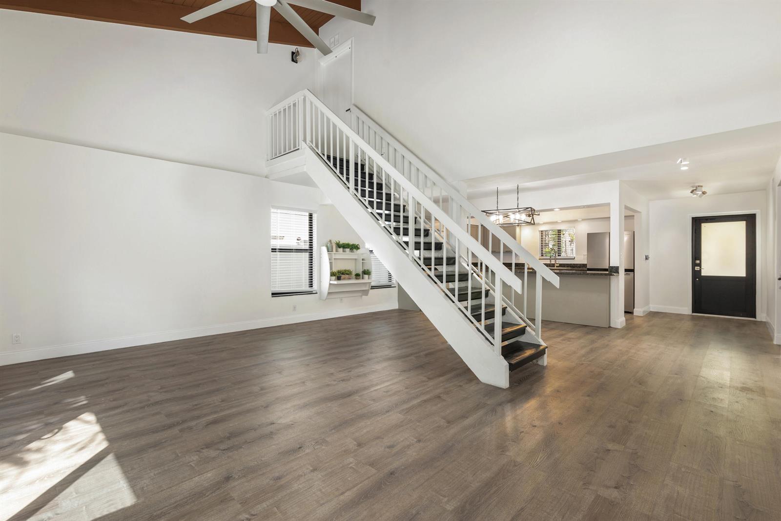 An open-concept living area features wood-look flooring, a white staircase, and a kitchen in back — 2474 Douglas Avenue, Delray Beach FL 33444, DELRAY BEACH, FL