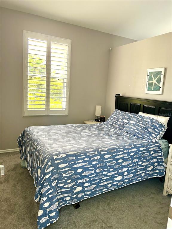 A bedroom features a bed with a blue fish-patterned quilt, plantation shutters, and gray carpeting — 17274 ASMARA COURT, PUNTA GORDA, FL