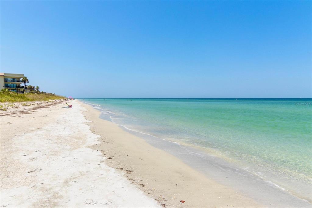 A sandy beach stretches along the turquoise ocean with a building visible in the distance — 1660 GULF BOULEVARD UNIT 607, CLEARWATER BEACH, FL