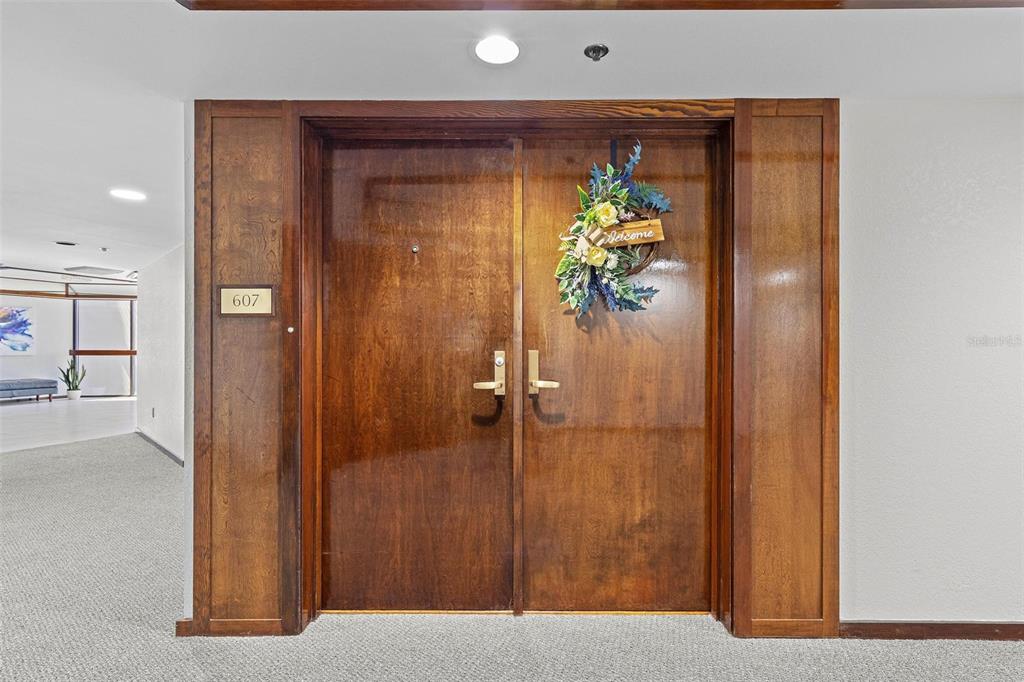 A set of double wooden doors with a welcome wreath marks the entrance to unit 607 — 1660 GULF BOULEVARD UNIT 607, CLEARWATER BEACH, FL