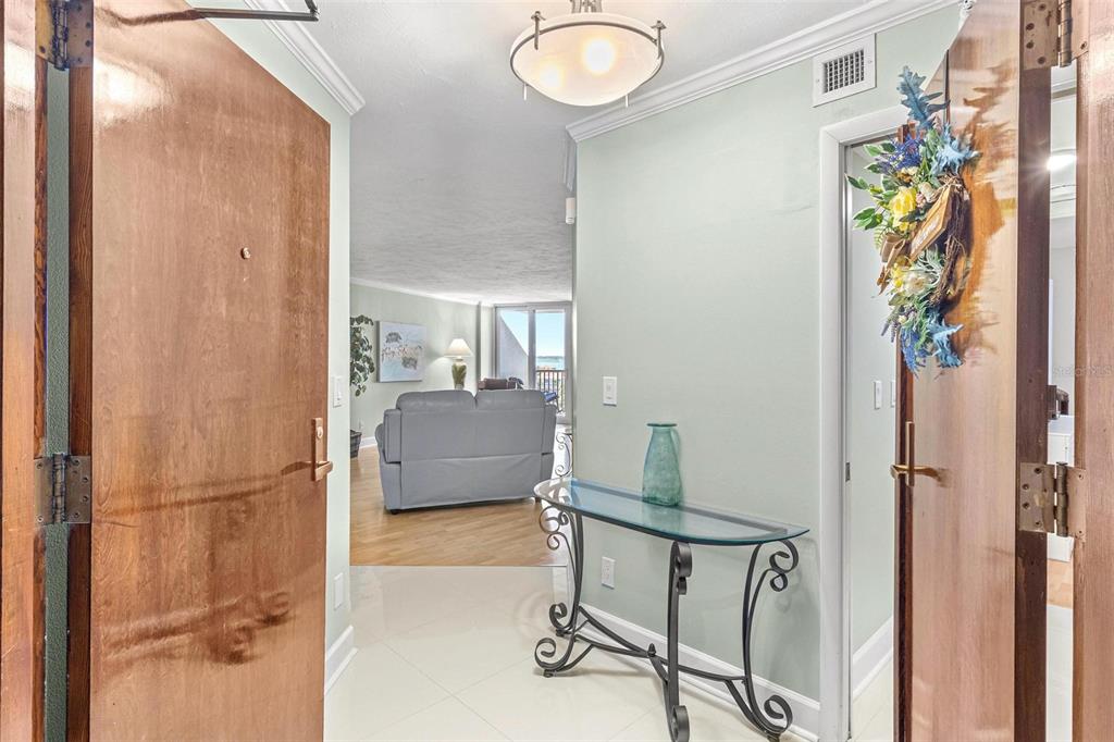 An entryway with a glass console table leads into a living room with ocean views — 1660 GULF BOULEVARD UNIT 607, CLEARWATER BEACH, FL