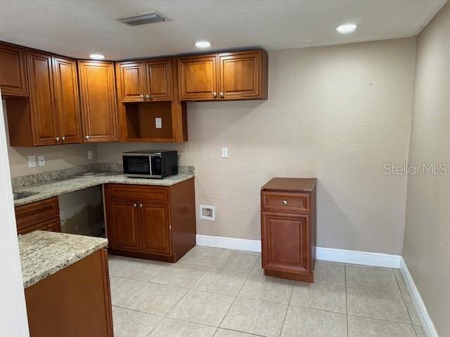 A kitchen features wood cabinets, granite countertops, a microwave, and light-colored tile flooring — 2847 W HARWOOD STREET, ORLANDO, FL