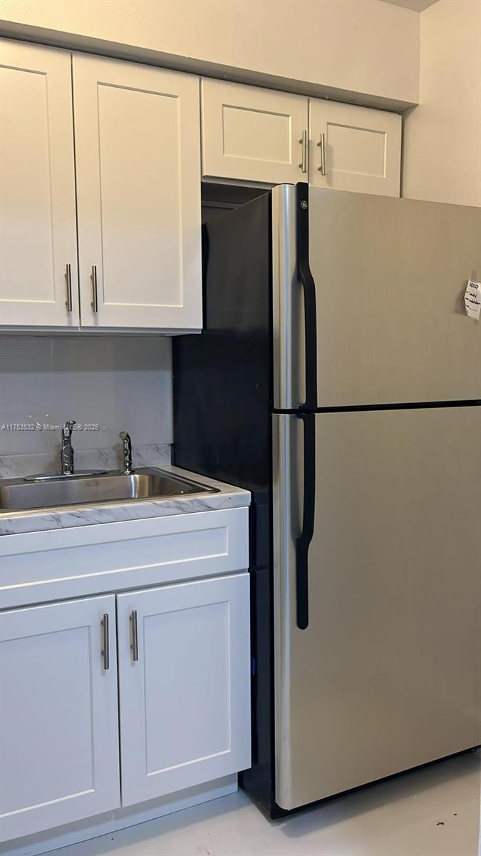 A kitchen features white cabinets, a stainless steel sink, and a stainless steel refrigerator — 550 NE 44th St # M2, Deerfield Beach FL 33064, DEERFIELD BEACH, FL