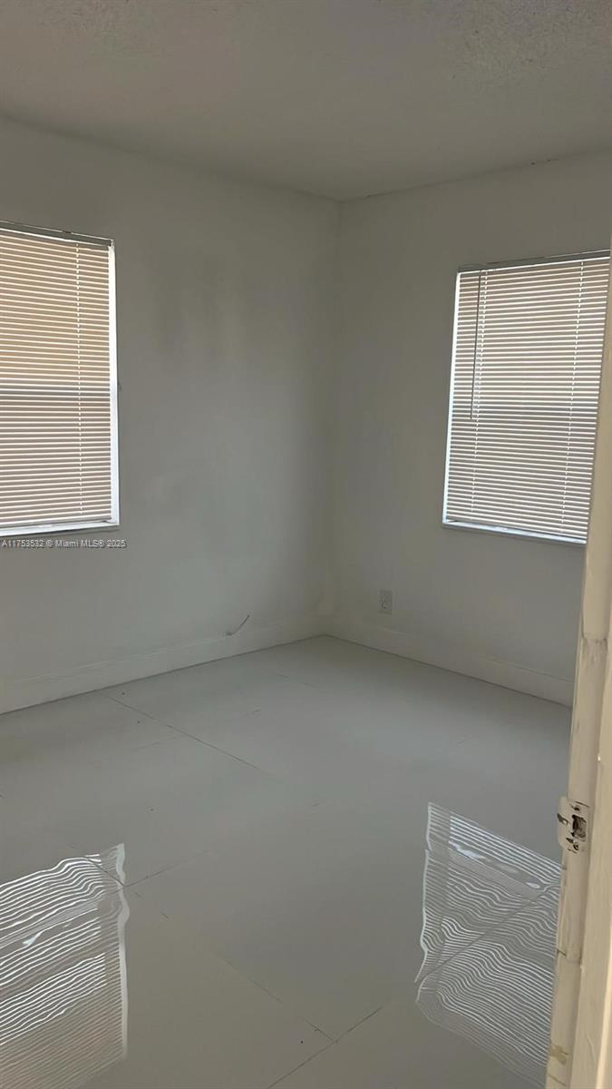 An empty room features white walls, white tile flooring, and two windows with blinds — 550 NE 44th St # M2, Deerfield Beach FL 33064, DEERFIELD BEACH, FL