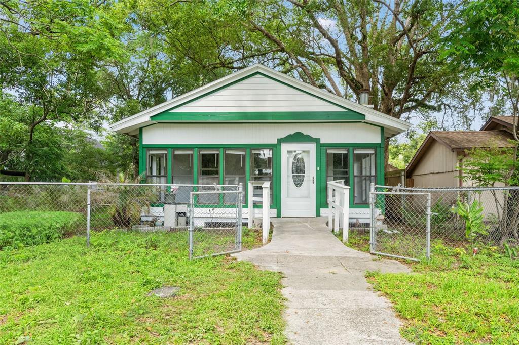 A small, white house with green trim and a screened porch sits behind a chain-link fence — 5518 11TH STREET, ZEPHYRHILLS, FL
